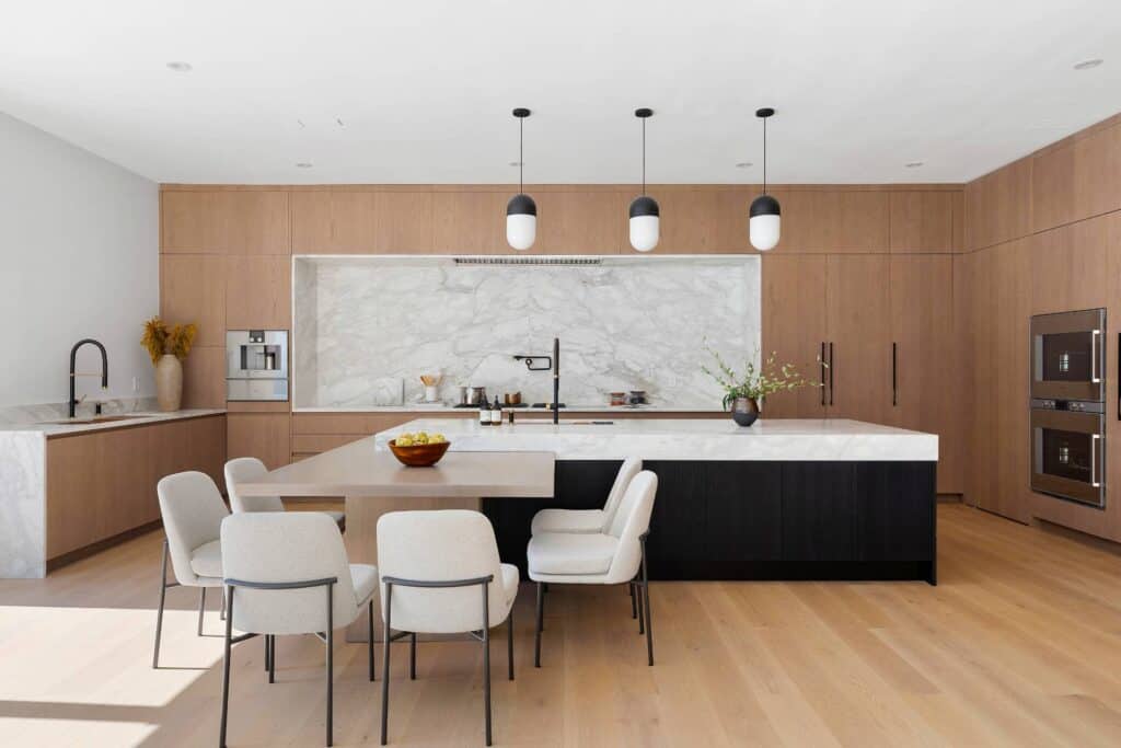 Contemporary kitchen with floor-to-ceiling wood panel cabinetry, large island with black base, marble backsplash, integrated appliances, and modern pendant lighting.